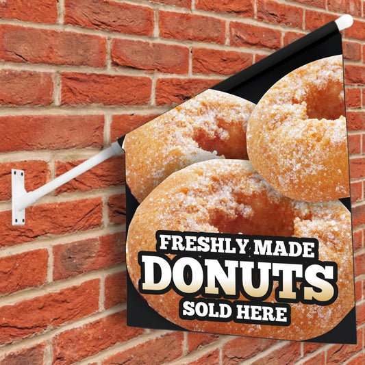 Donut-themed wall flag with 'Freshly Made Donuts Sold Here' text against a brick wall.